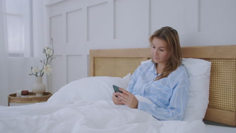 Attractive-young-beautiful-girl-chatting-with-her-friends--while-sitting-on-her-bedroom.-Young-woman-lying-in-bed-and-holding-smartphone